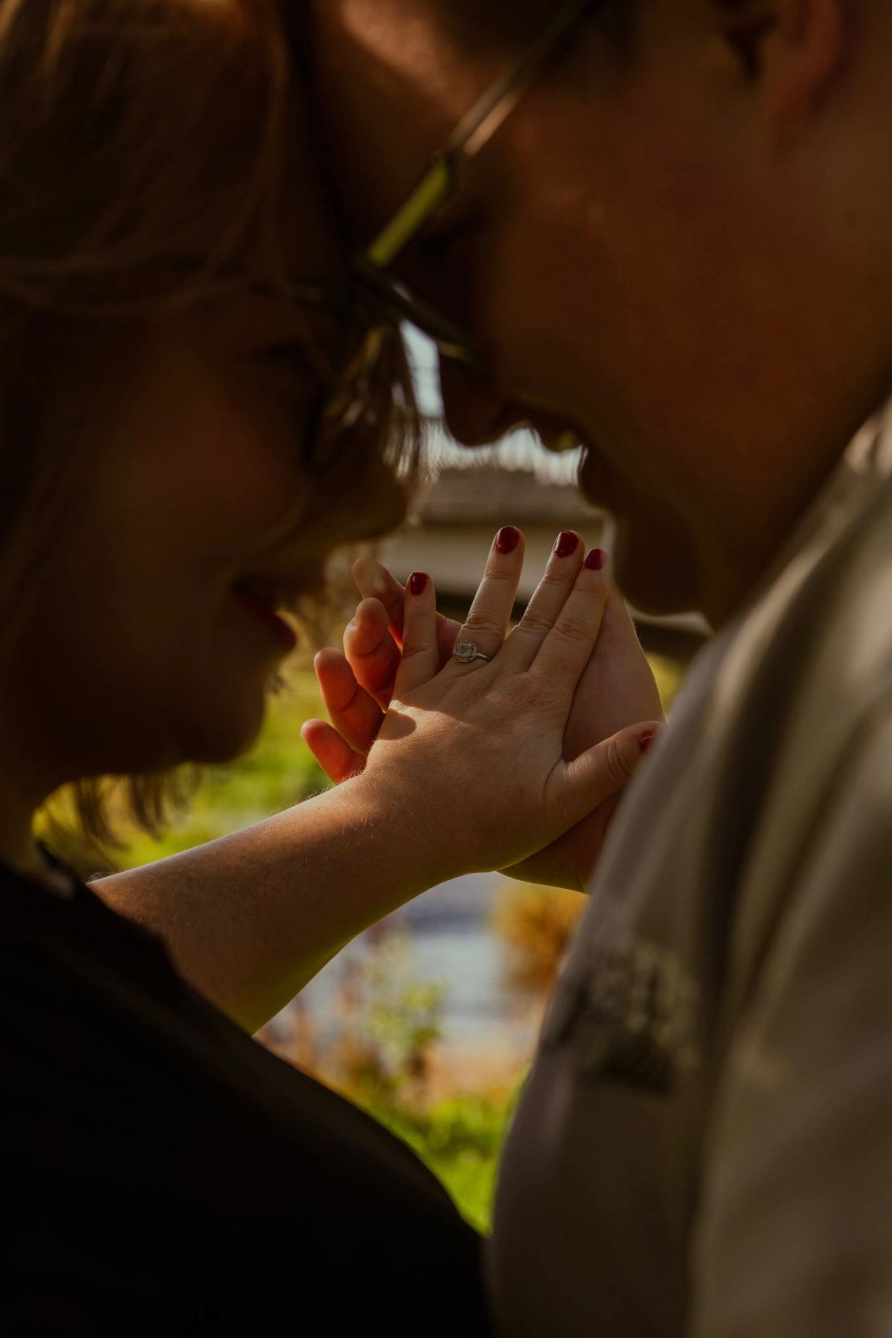 Engaged couple foreheads together, showing the engagement ring in golden light