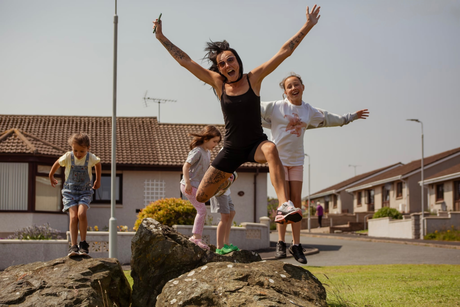 Family leaping off rocks together on a sunny street